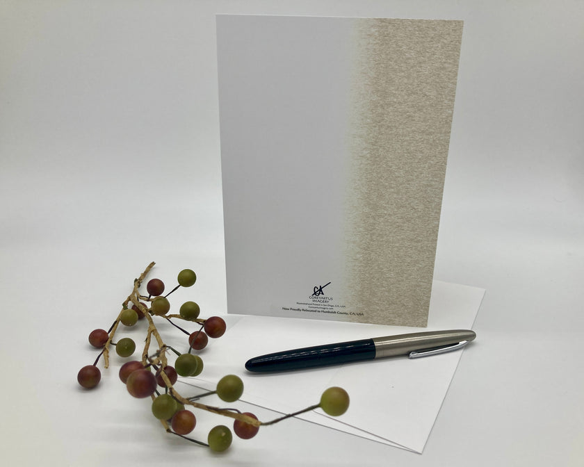 Back of a greeting card displayed with a pen, and decorative branch on a white surface