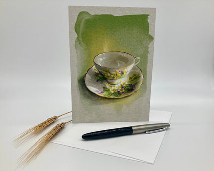 Greeting card with a teacup design on a white surface with a pen and wheat stalks.