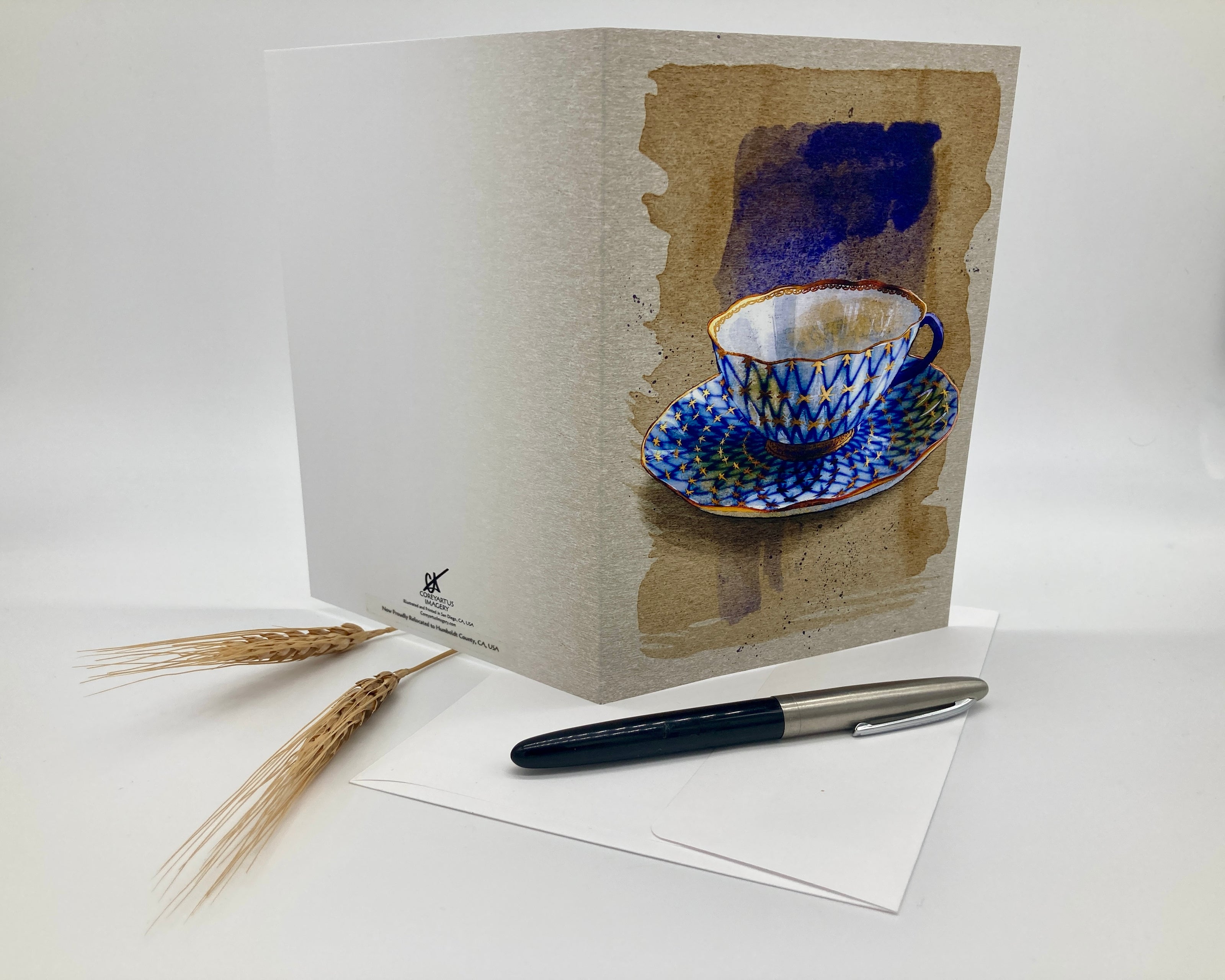 Greeting card with a blue teacup design, pen, and wheat stalks on a white background