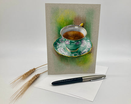 Greeting card with a tea cup illustration on a white surface with a pen and straw.