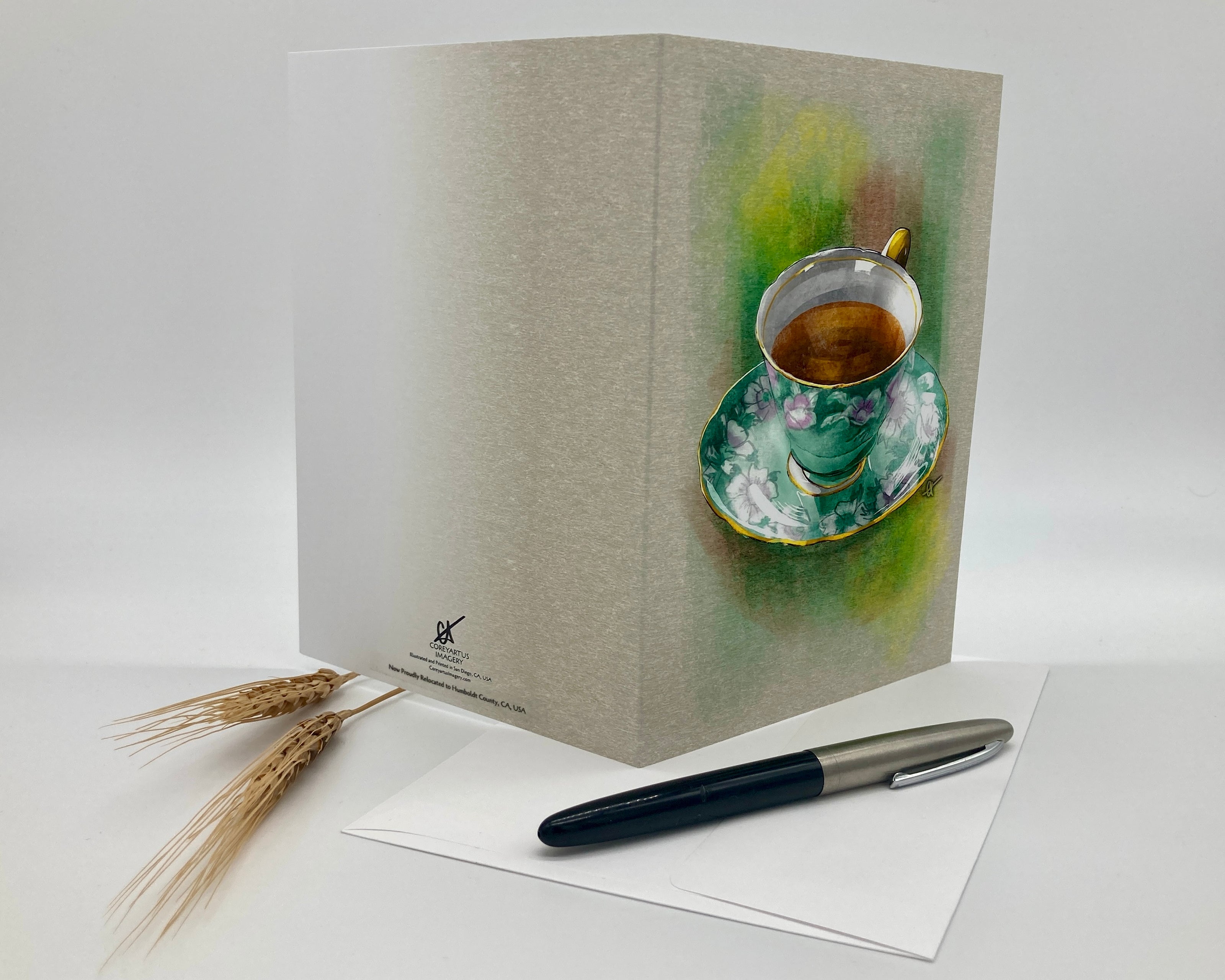 Greeting card with a tea cup design on a white surface with a pen and paper.