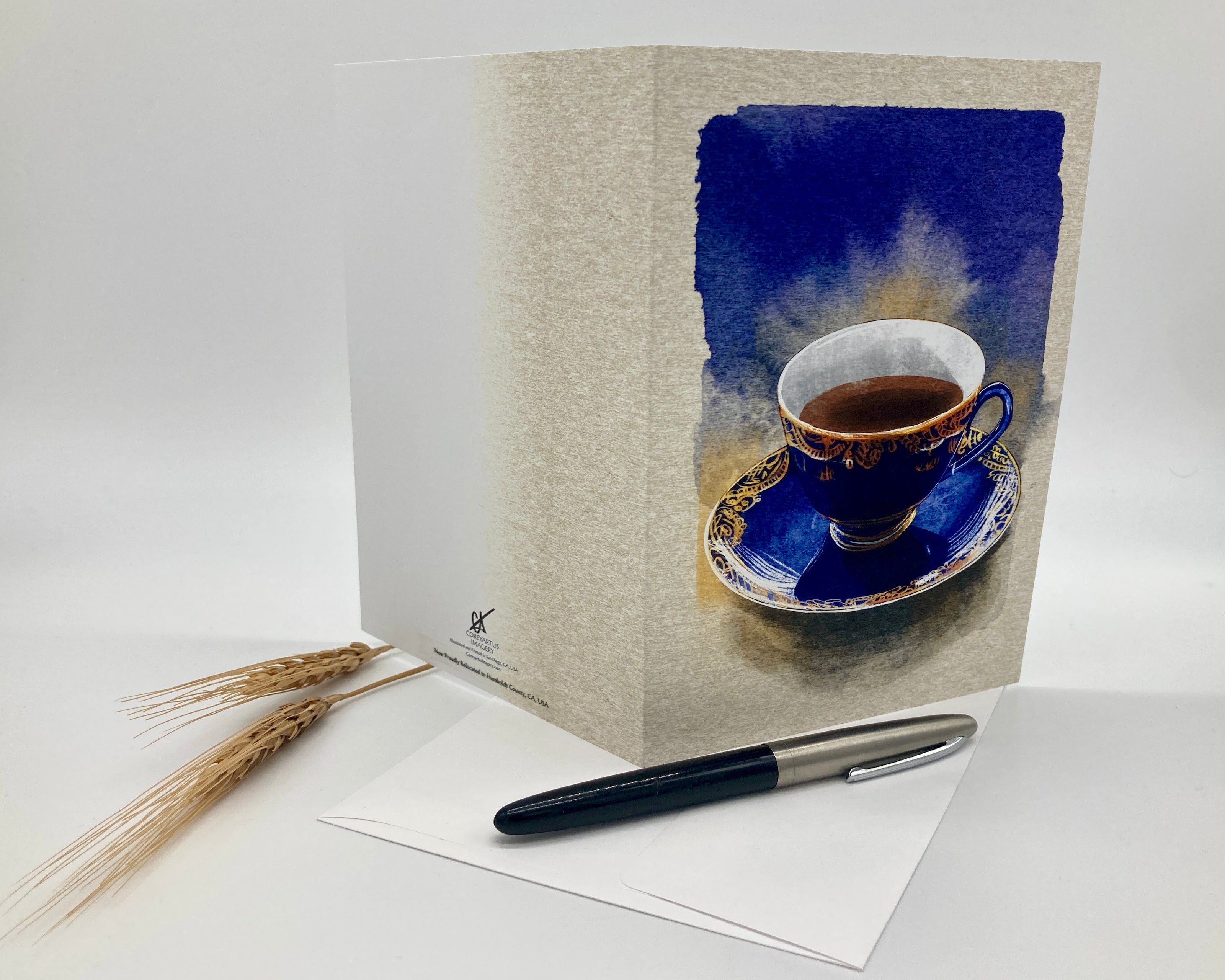 Greeting card with a blue cup design, pen, and paper on a white background