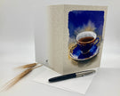 Greeting card with a blue cup design, pen, and paper on a white background