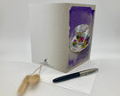 Greeting card with a floral teacup design on a white surface with a pen and decorative item.