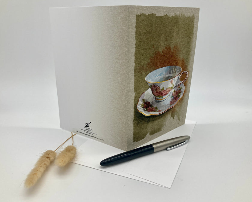 Greeting card with a teacup design, pen, and decorative item on a white background