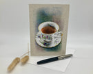 Greeting card with a teacup illustration on a textured background, accompanied by a pen and decorative item.
