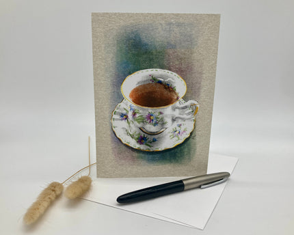 Greeting card with a teacup illustration on a textured background, accompanied by a pen and decorative item.