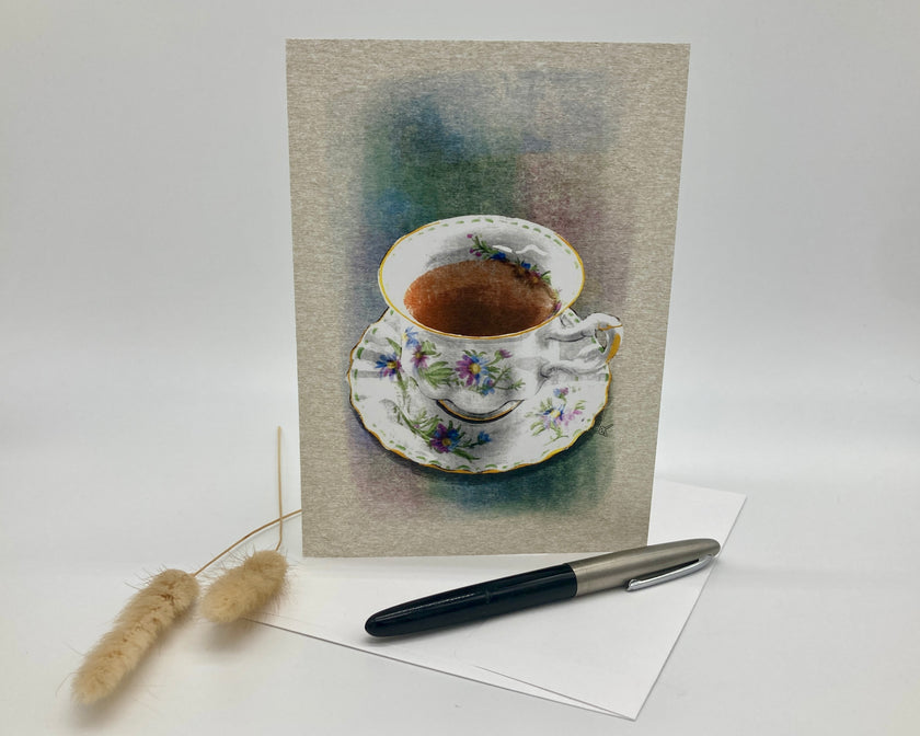 Greeting card with a teacup illustration on a textured background, accompanied by a pen and decorative item.
