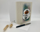 Greeting card with a teacup design on a white surface with a pen and decorative item.