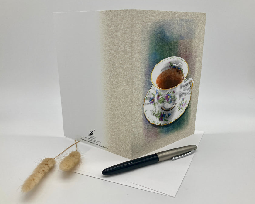 Greeting card with a teacup design on a white surface with a pen and decorative item.