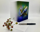 Greeting card with a bird design on a white surface with berries and a pen.