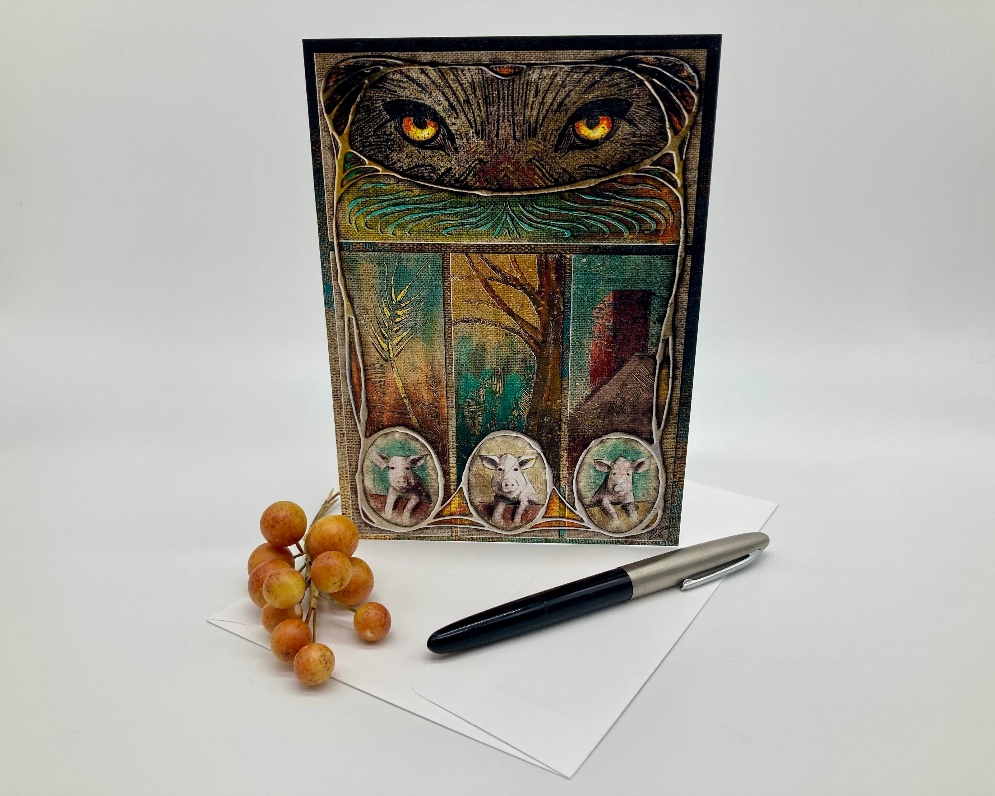 Greeting card with artistic design featuring a cat's face and three small images of animals, accompanied by a pen and dried fruits on a white background.