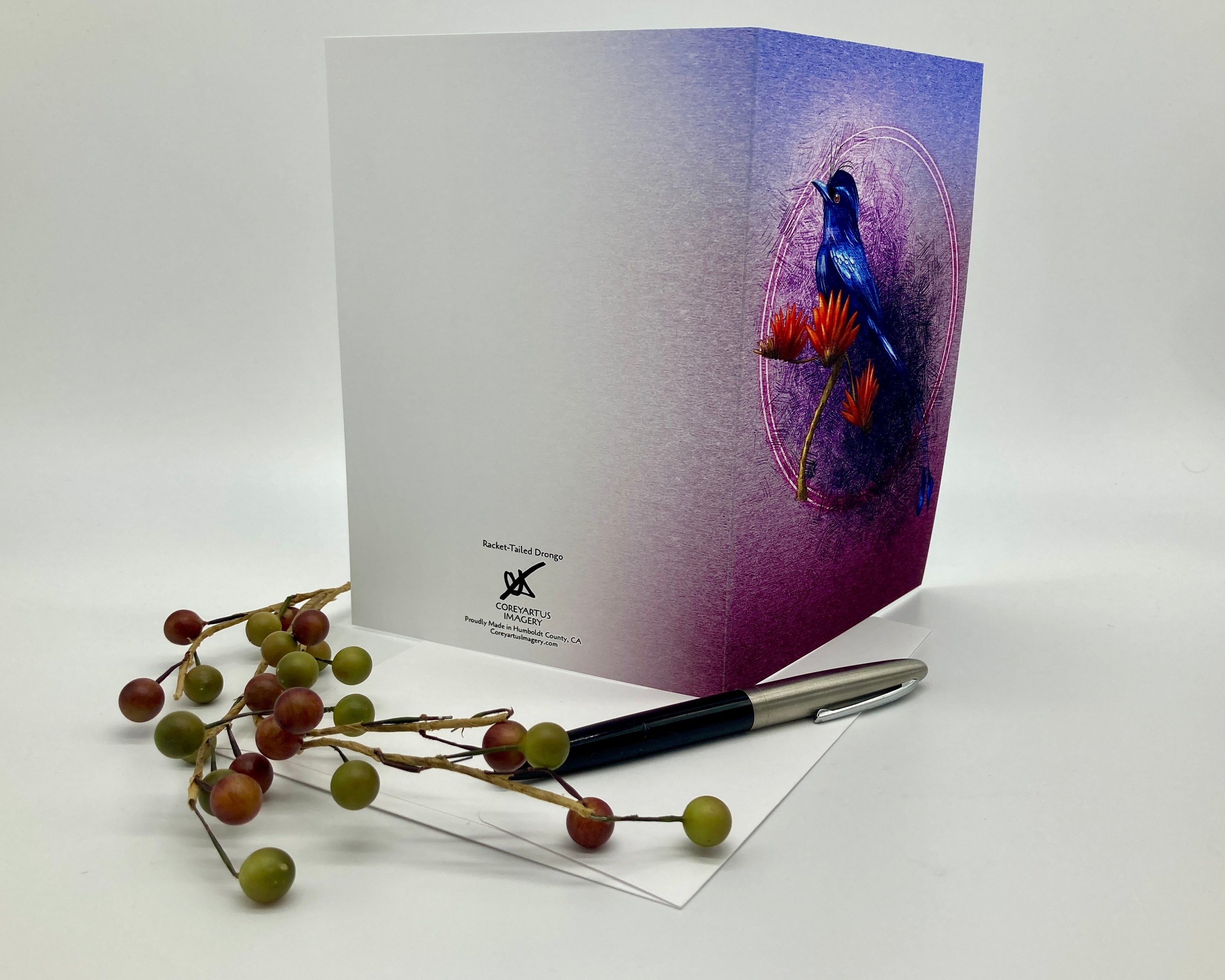 Greeting card with a colorful bird design on a white surface with a pen and decorative branches.