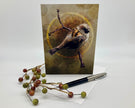 Greeting card with a bird illustration on a branch, surrounded by berries and a pen.