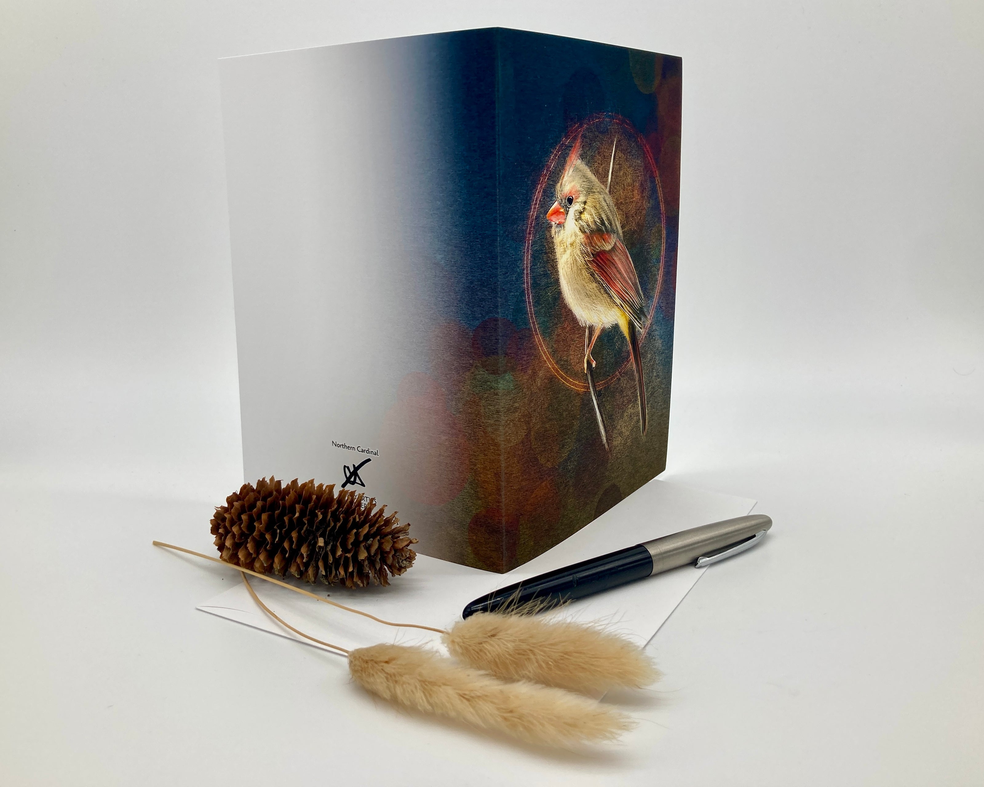 Open greeting card with bird illustration on cover, pen, and decorative elements on white background