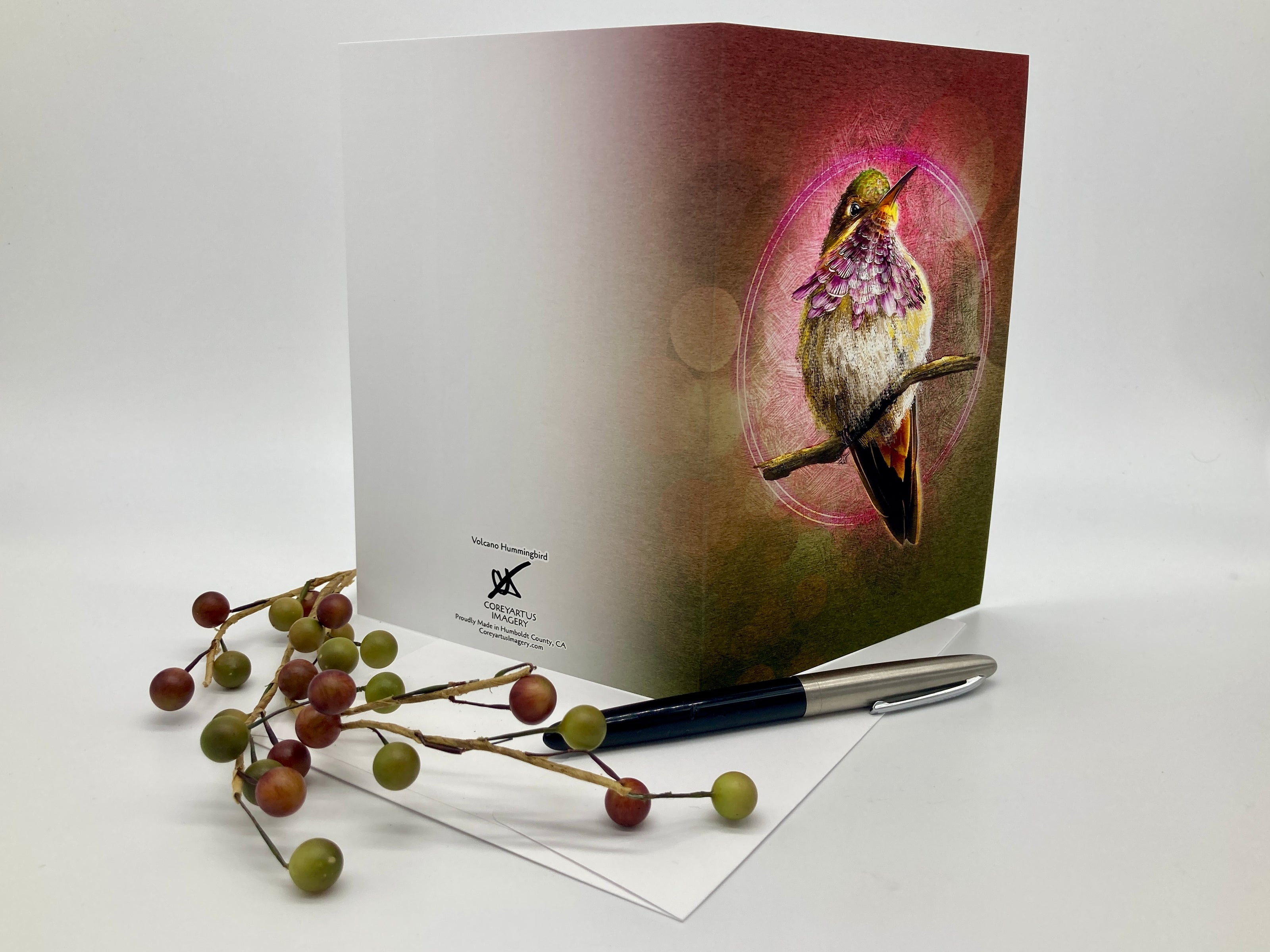 Greeting card with a bird design on a white surface with berries and a pen.