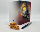 Greeting card with a robin design on a white surface with berries and a pen.