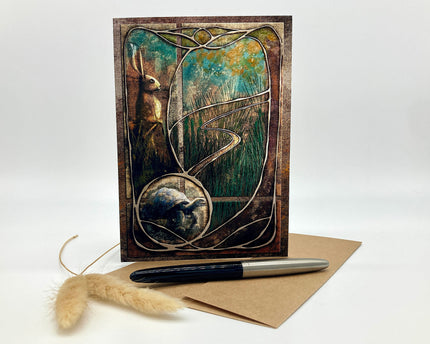 Greeting card with artistic design of a rabbit and tree, accompanied by a pen and envelope on a white background.