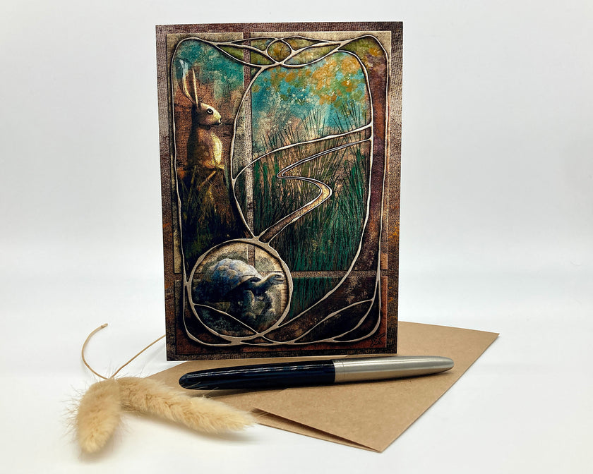 Greeting card with artistic design of a rabbit and tree, accompanied by a pen and envelope on a white background.