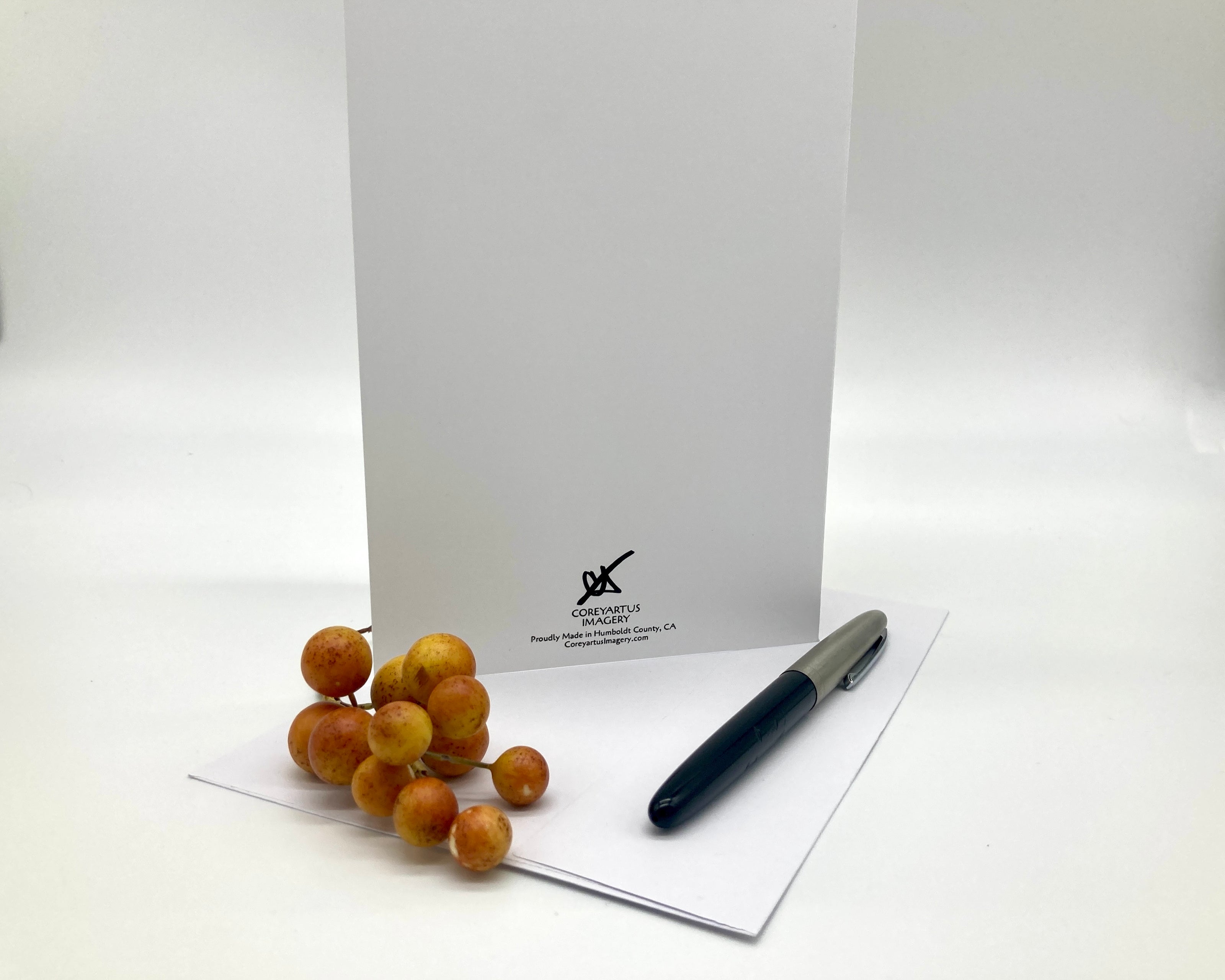 White card with a logo, pen, and small fruit on a white background