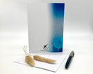 Back of a greeting card with a blue watercolor design, pen, and dried plant on a white background