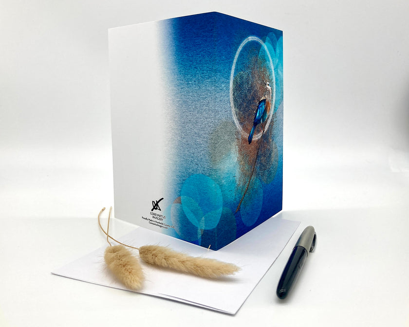 Open greeting card with a blue cover featuring a bird design, accompanied by a feather and pen on a white background.