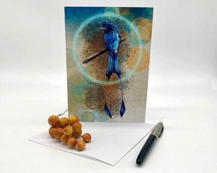 Greeting card with a blue bird design on a white surface with berries and a pen.