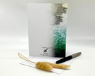 Greeting card with nature-themed design, pen, and feather on a white background