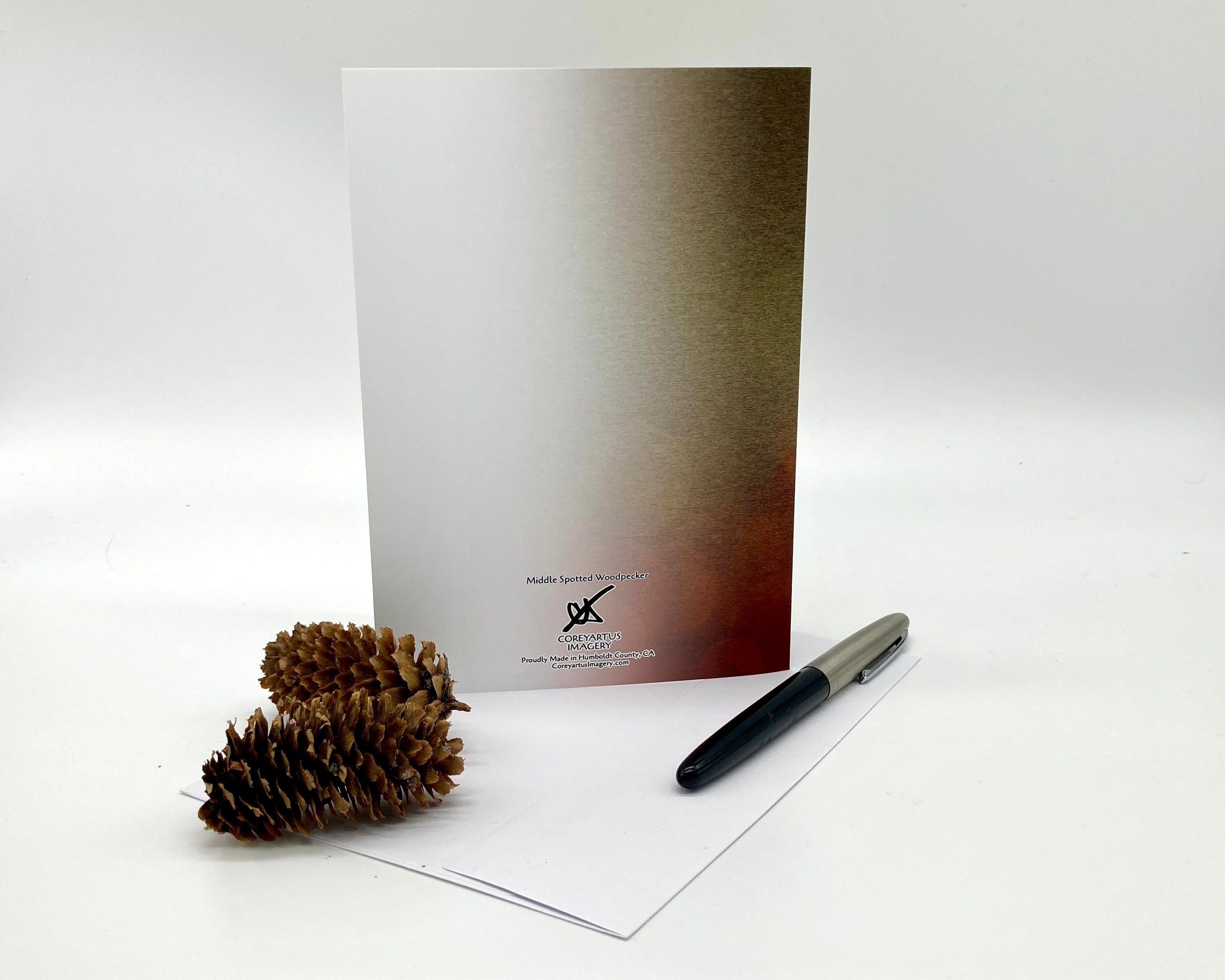 Back of a greeting card, pen, and pine cone on a white surface