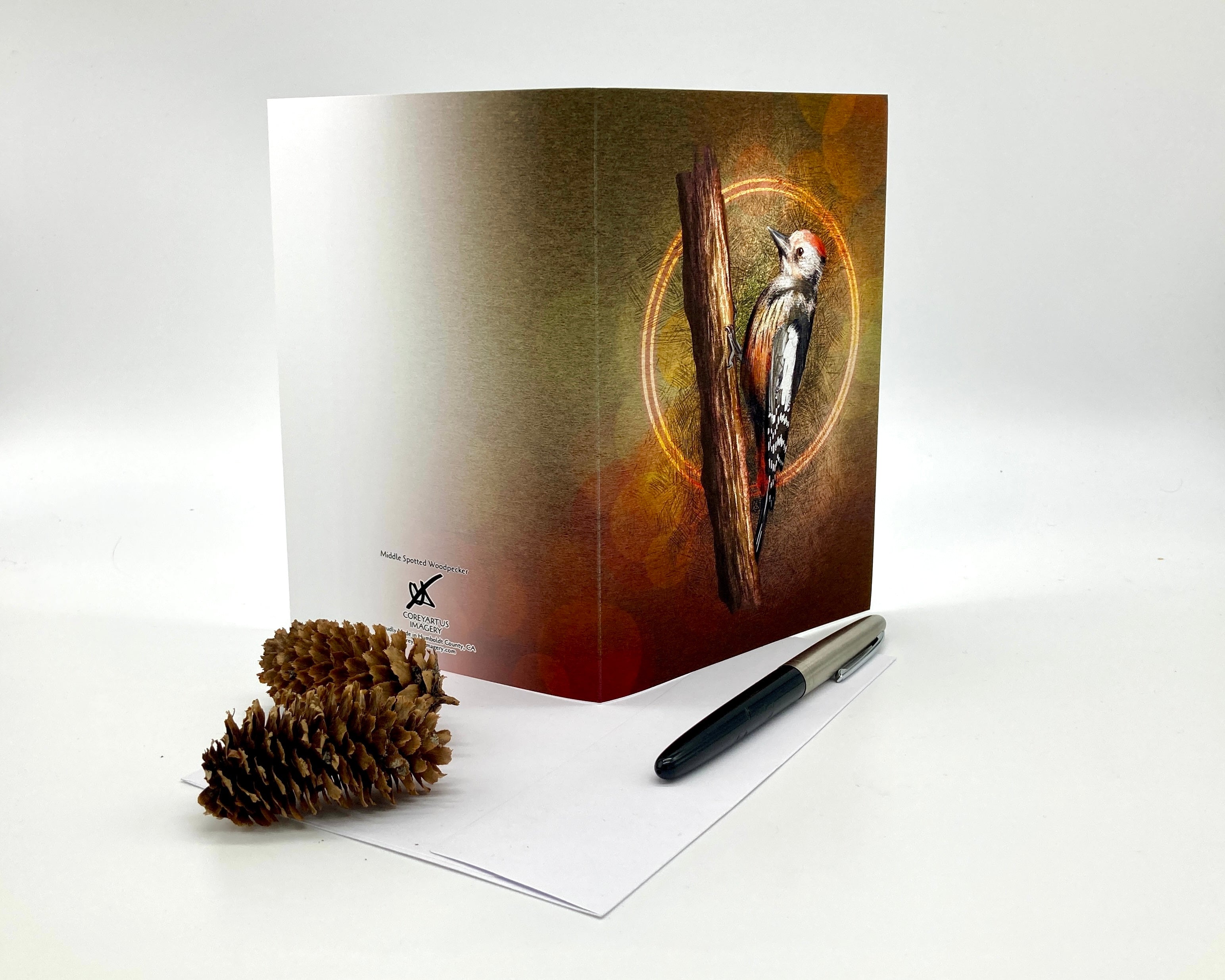 Greeting card with a bird design on a white surface with a pen and pine cone.
