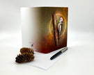 Greeting card with a bird design on a white surface with a pen and pine cone.