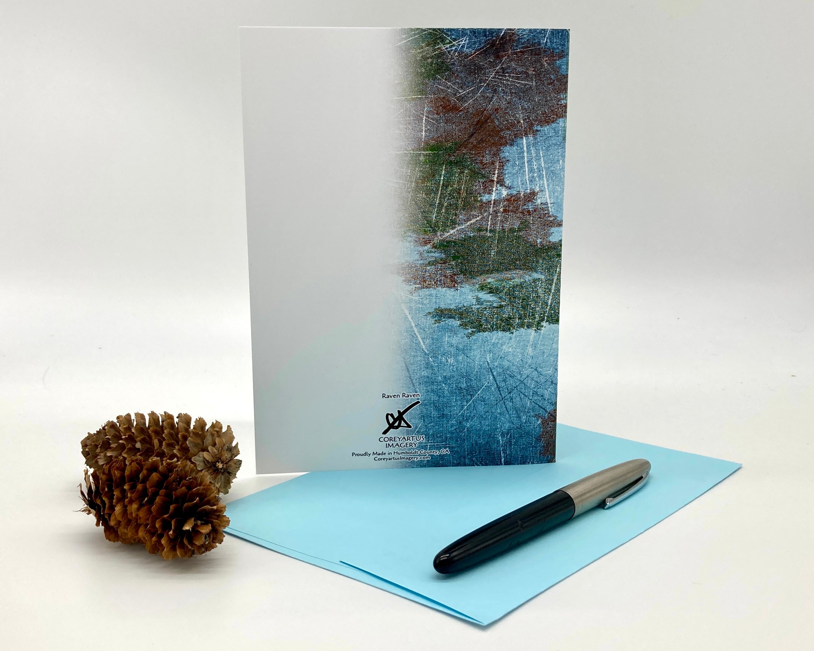 Greeting card with nature-themed design, pen, and pine cone on a white background