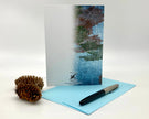 Greeting card with nature-themed design, pen, and pine cone on a white background