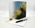 Greeting card with a bird design on a white surface with a pen and shell.