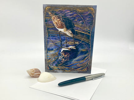 Decorative greeting card with a bird design on a white surface with a pen and shell.