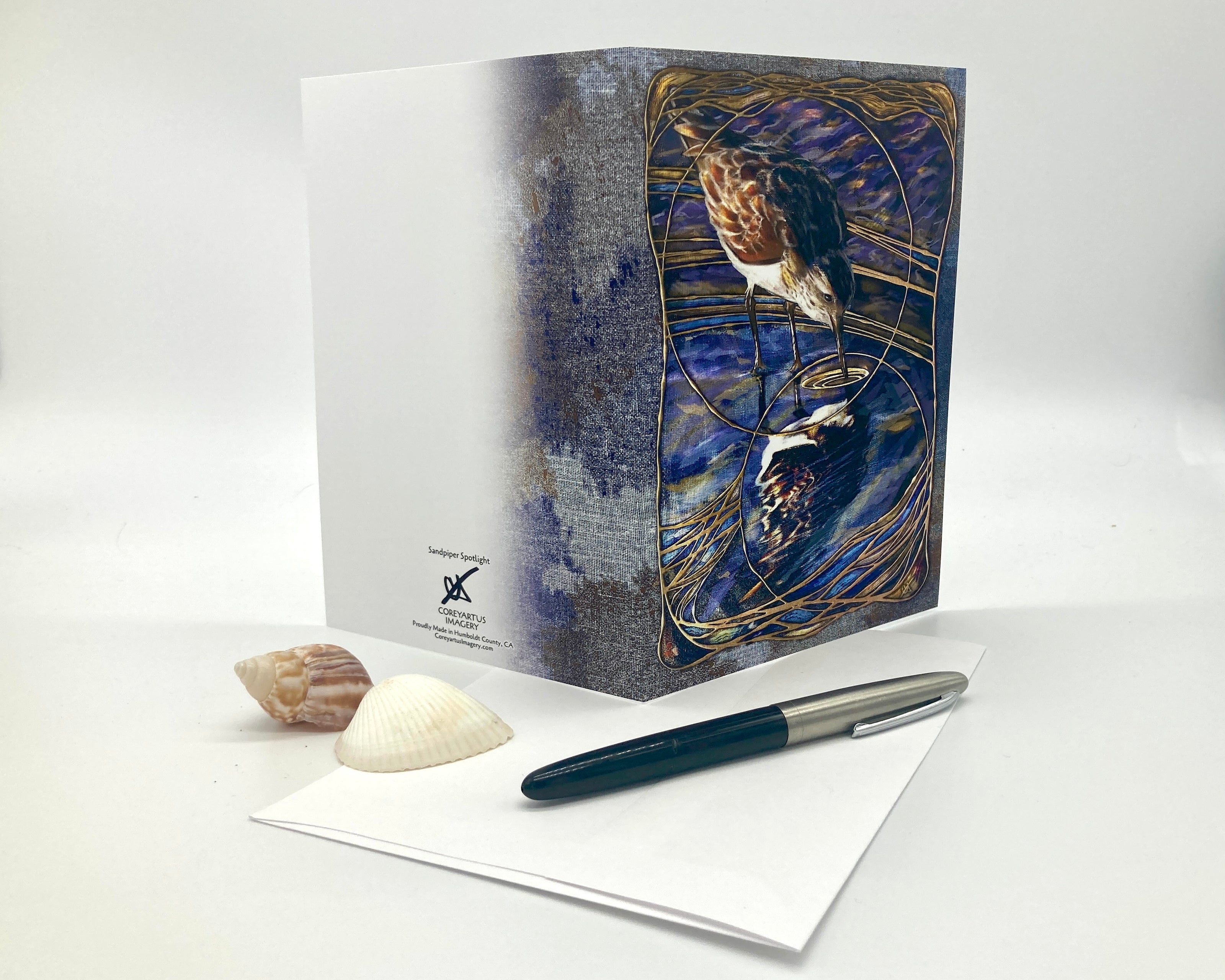 Greeting card with artistic design on a white surface with a pen and shells.