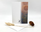 Greeting card with a patterned design on a white background, accompanied by dried plants and a pine cone.