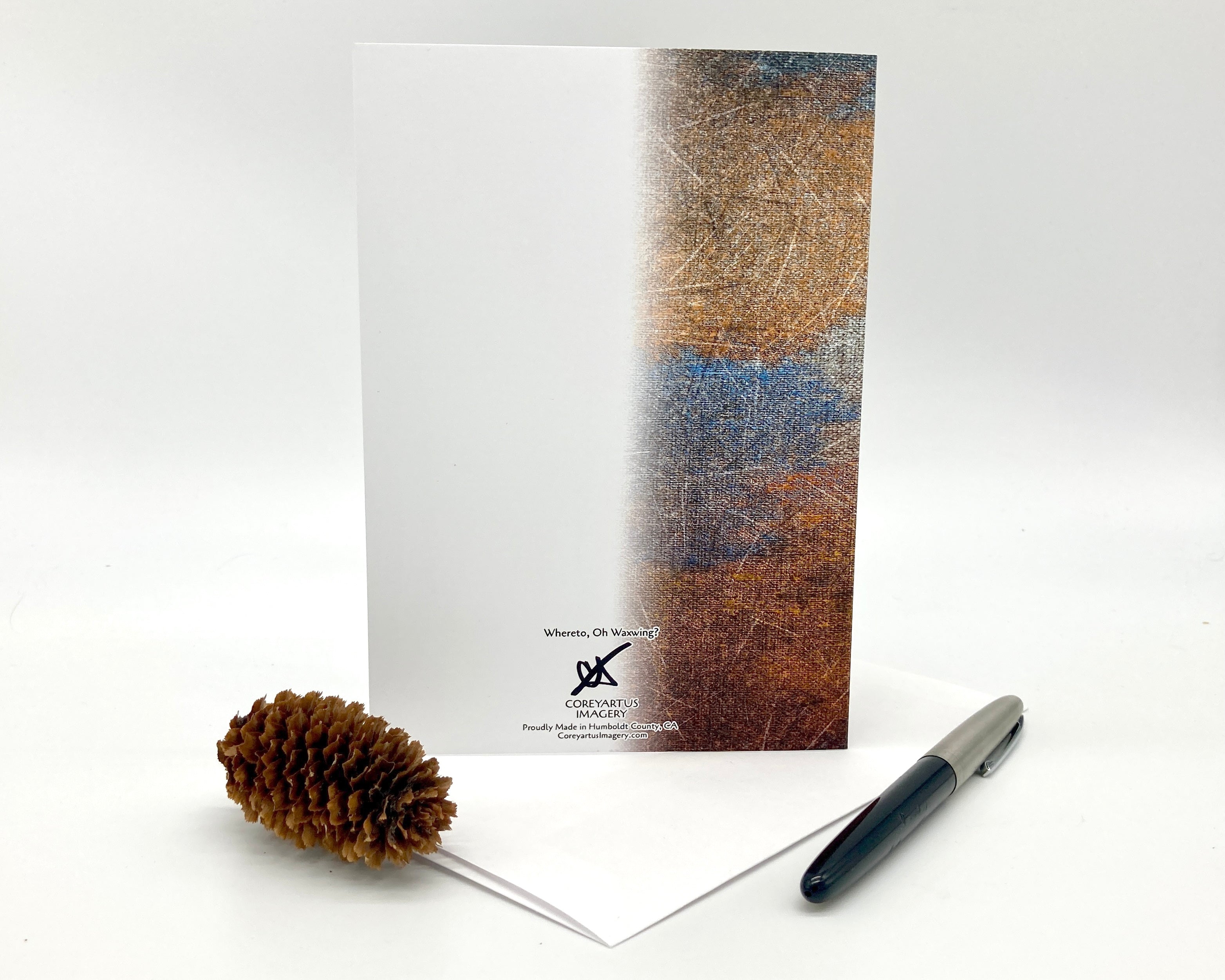 Greeting card with textured cover, pen, and pine cone on a white background