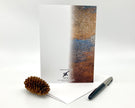 Greeting card with textured cover, pen, and pine cone on a white background