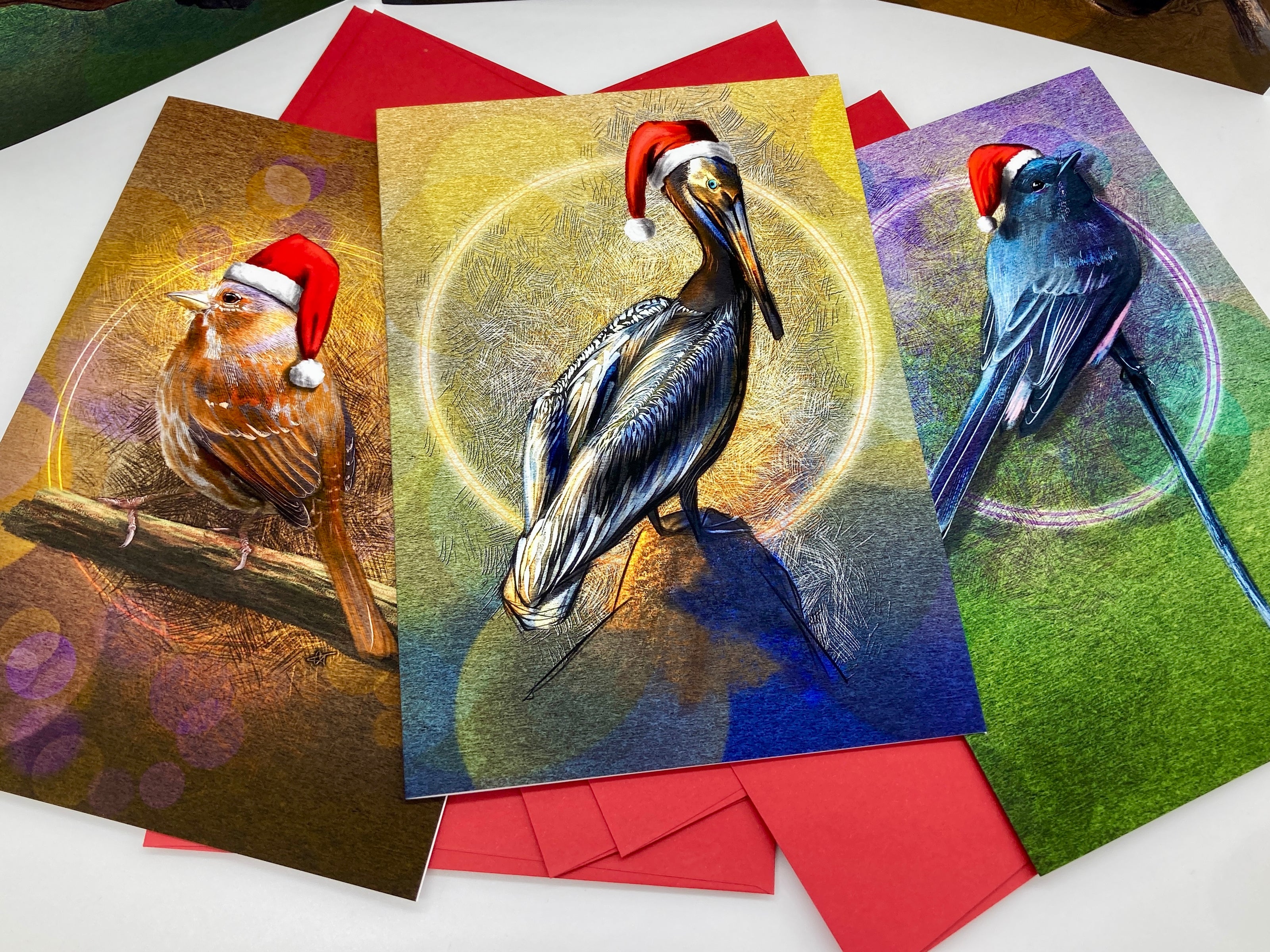 Three Christmas-themed greeting cards with birds wearing Santa hats on a white surface.