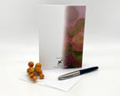 Note card with floral design, pen, and small fruit on a white background