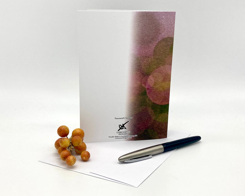 Note card with floral design, pen, and small fruit on a white background