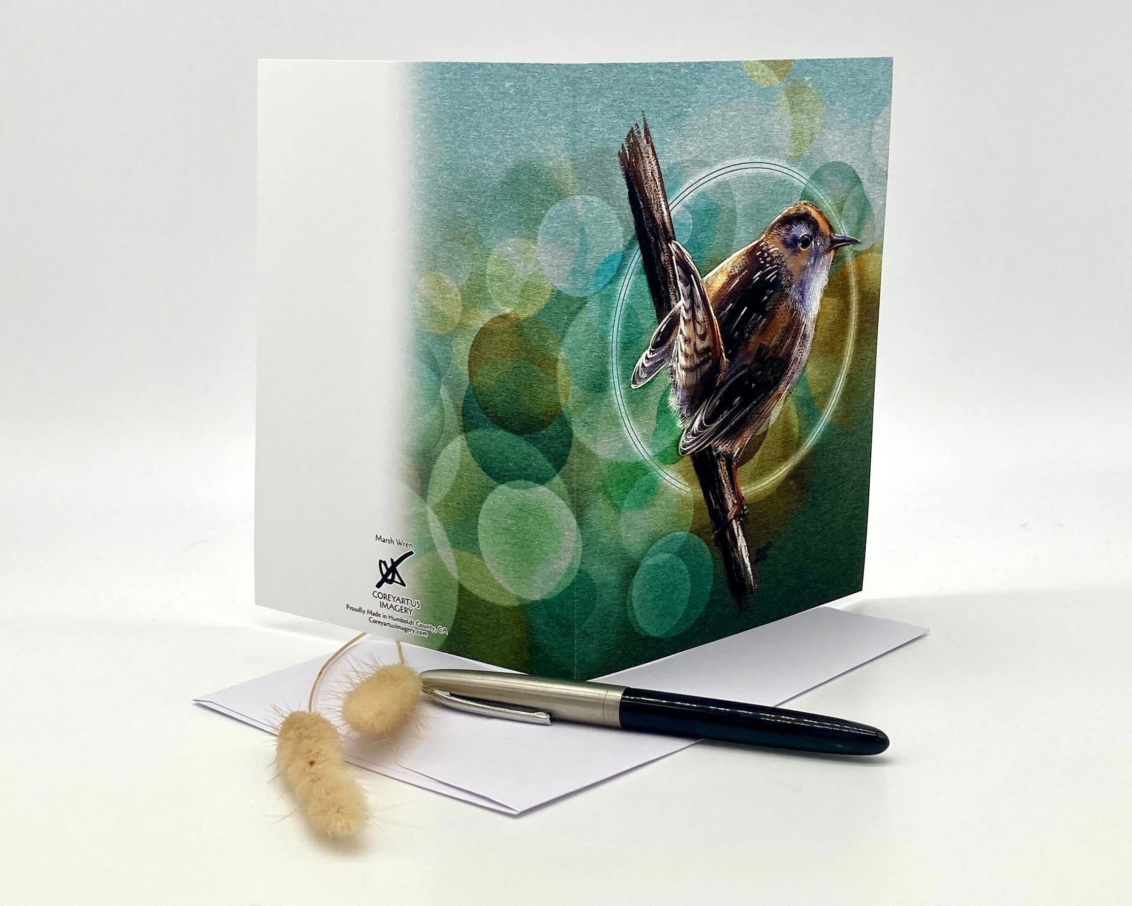 Greeting card with a bird design on a white surface with a pen and small object.