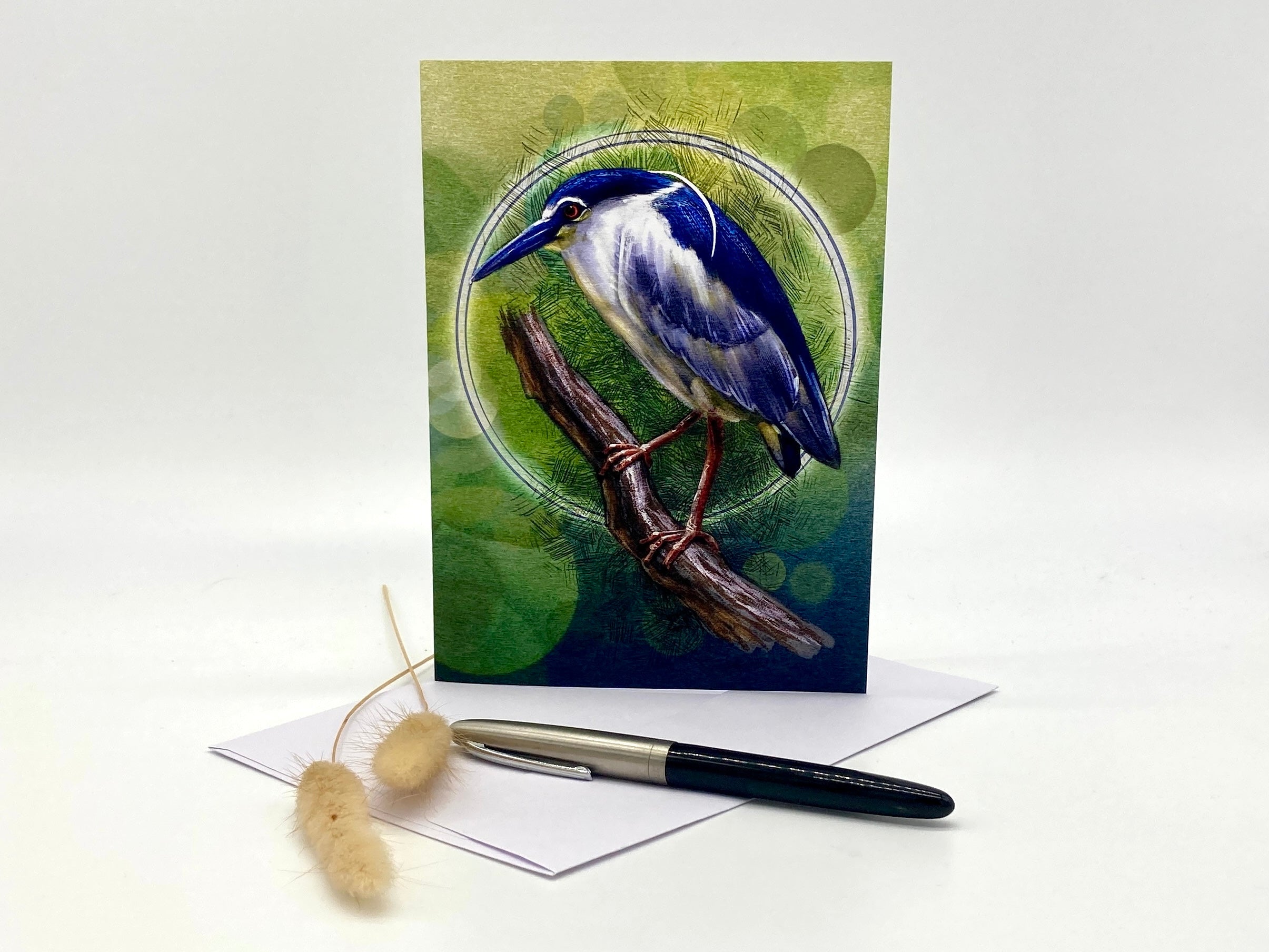 Greeting card with a blue bird illustration on a green background, accompanied by a pen and decorative items.