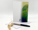Greeting card with green abstract design, pen, and decorative items on a white background
