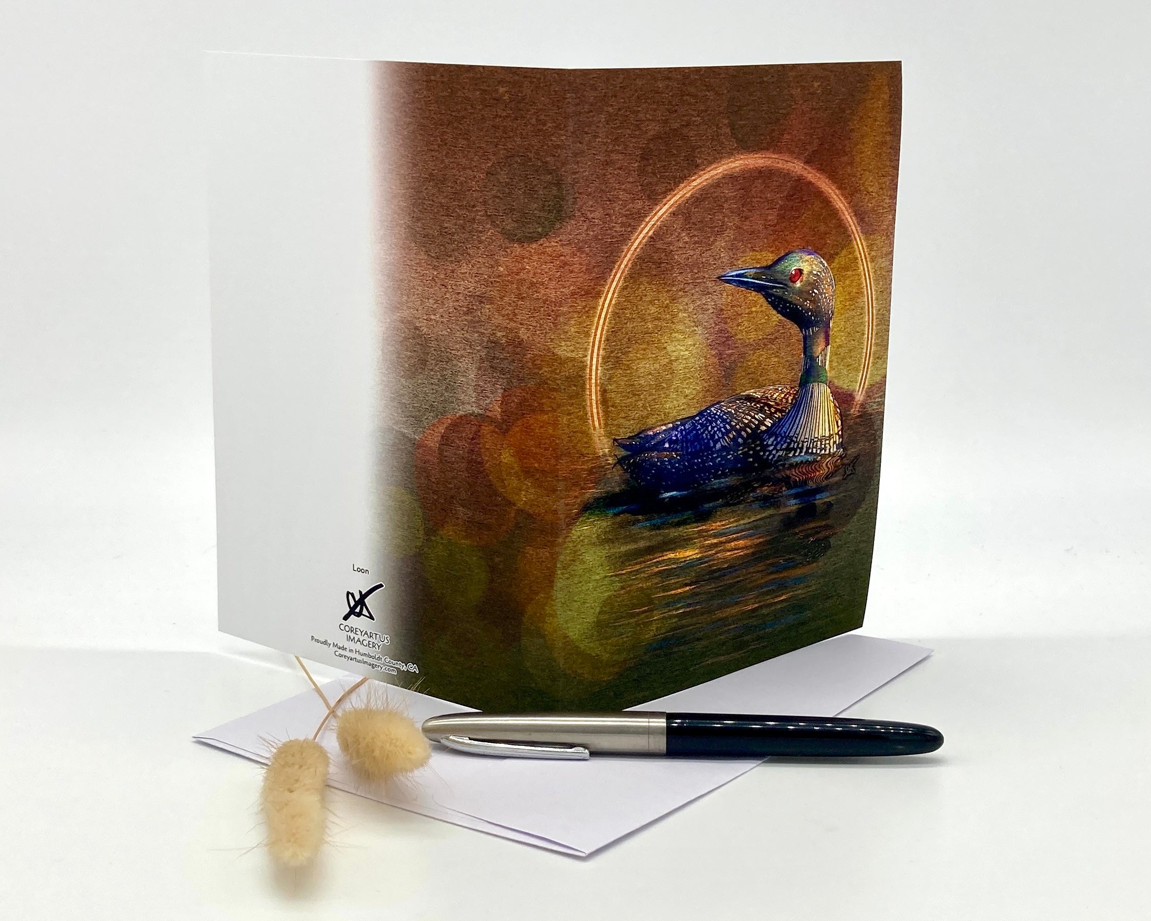 Greeting card with a loon design on a white surface with a pen and decorative items.