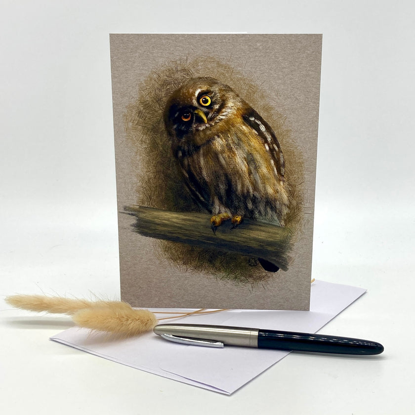 Greeting card with an owl illustration on a wooden branch, accompanied by a pen and dried grass.