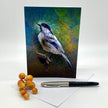 Greeting card with a bird illustration on a white surface with berries and a pen.