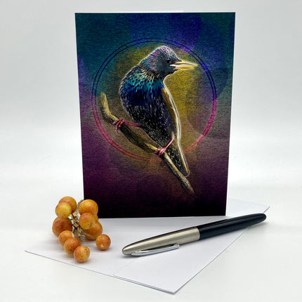 Greeting card with a stylized bird illustration on a branch, placed on a white surface with a pen and grapes.