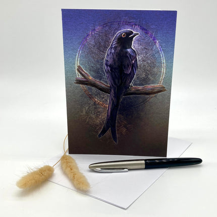 Greeting card with a purple bird illustration on a branch, accompanied by a pen and decorative items.